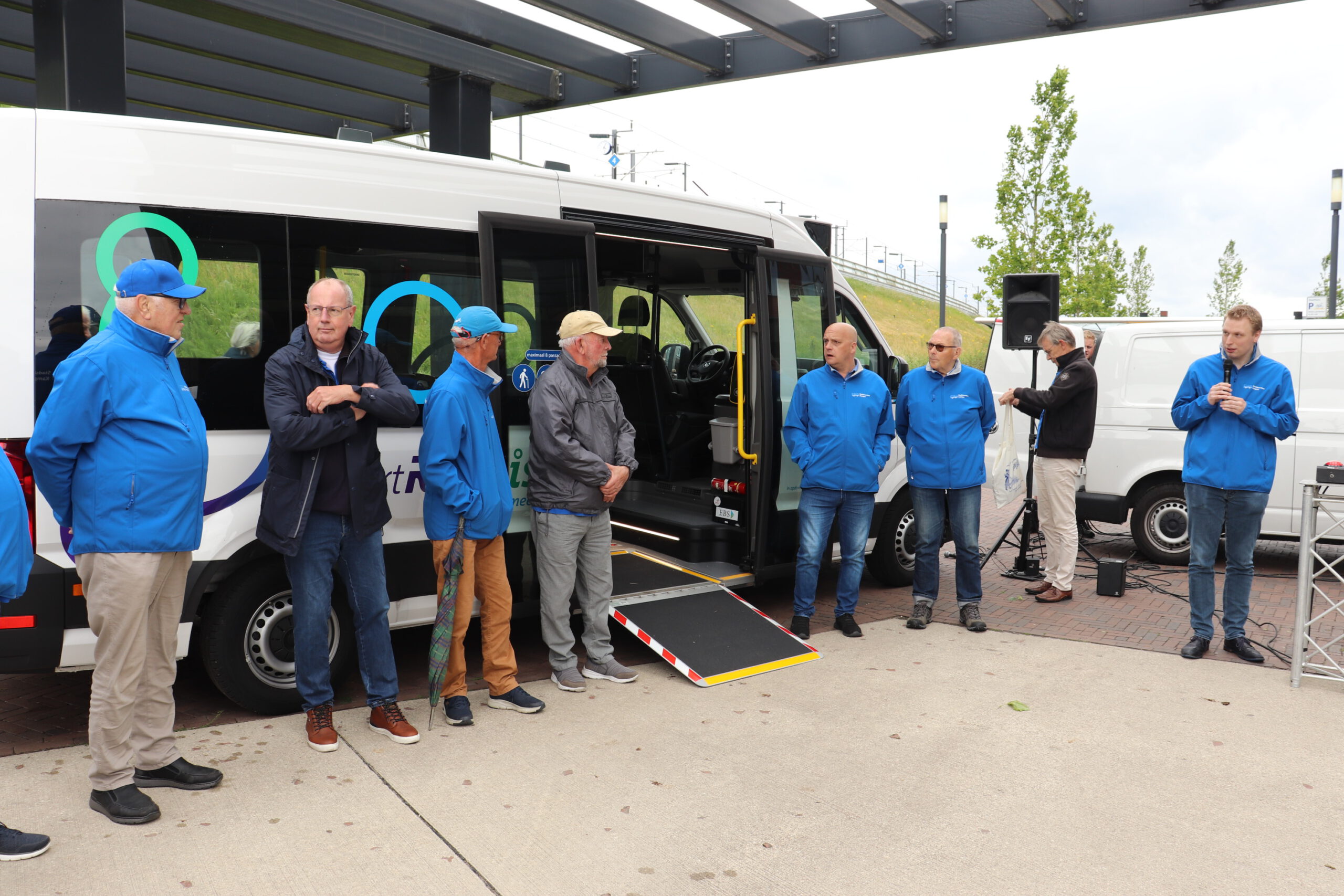 Vrijwillige chauffeurs bij de nieuwe bus met de uitgeklapte rolstoeloprijplaat.